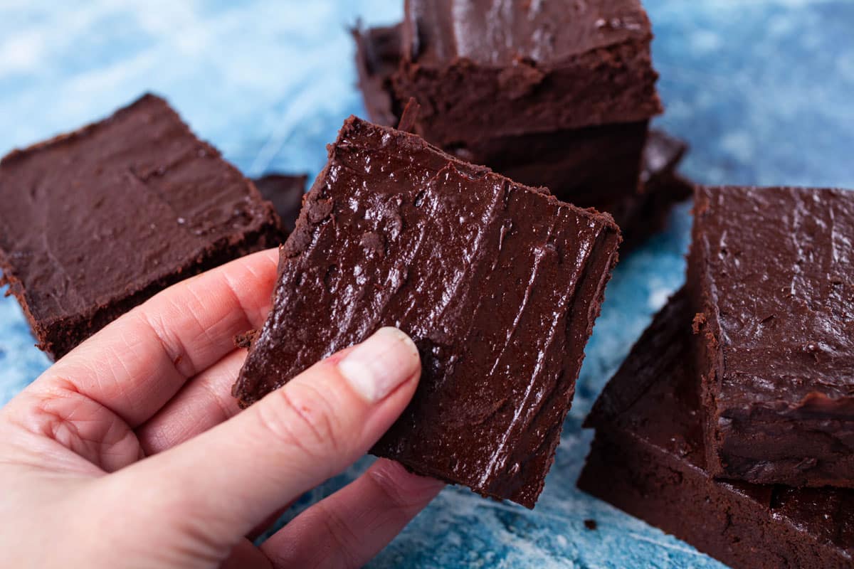 A hand holding a no flour brownie with a shiny crust.