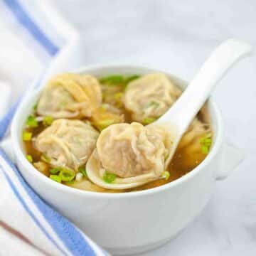 Wonton soup with green onions served in a mini bowl.