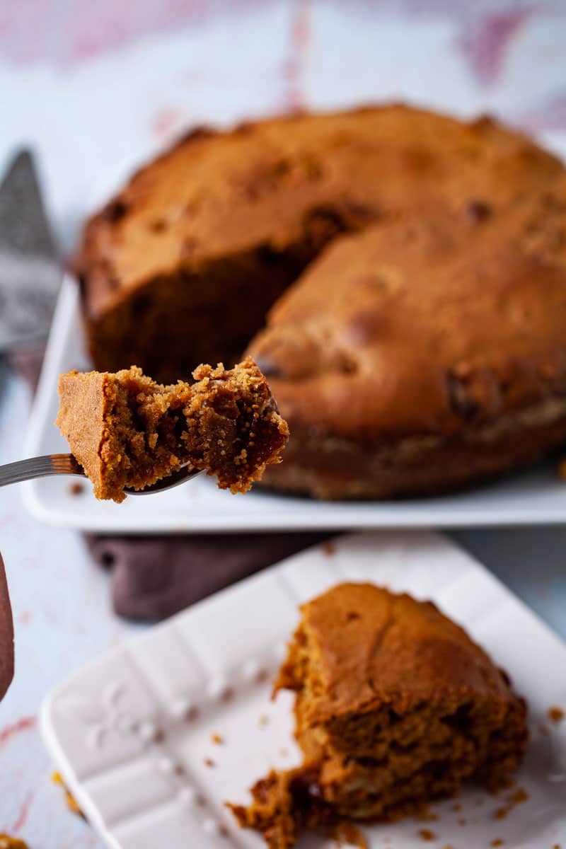 A fork lifting a piece of a cake above a plate with the coffee cake in the background.