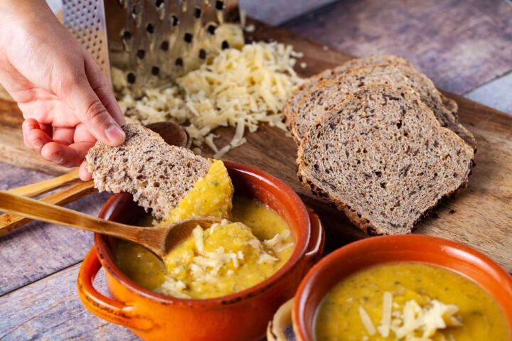 A child's hand dipping a piece of bread in a bowl filled with creamy squash-zucchini soup.