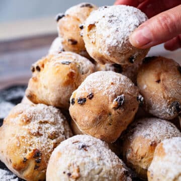 A hand grabbing an Italian doughnut from a large stack topped with sugar powder.