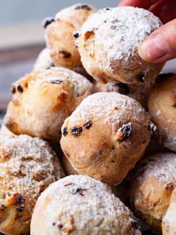 A hand grabbing an Italian doughnut from a large stack topped with sugar powder.