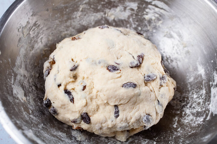 A ball of dough filled with raisins resting in a stainless steel bowl.