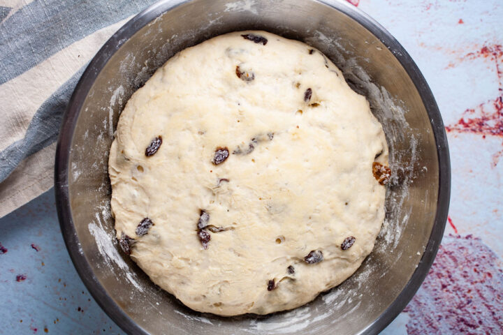 A ball of risen dough filled with raisins resting in a stainless steel bowl.