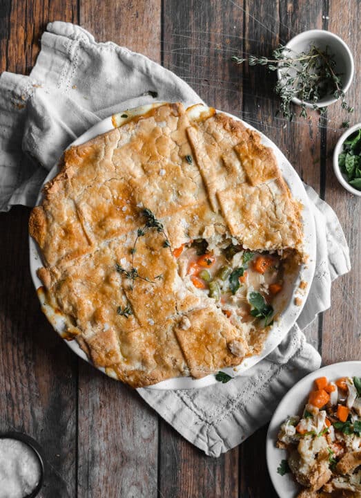 an overhead shot of a pie plate filled with chicken pot pie on a white napkin with one slice missing from the pie.