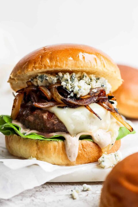 a bison burger on a bun with lettuce, melty cheese, caramelized onions and blue cheese.