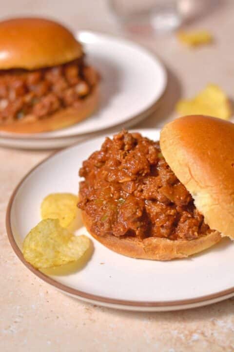 bison slopping joe on a white plate with some potato chips on the side.