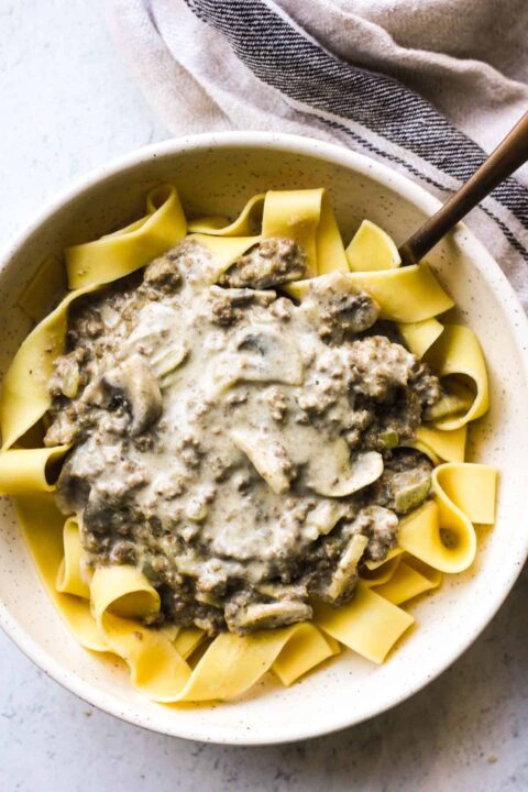 an overhead shot of bison stroganoff piled on a bed of egg noodles in a white bowl.