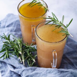 Two cups filled with broth and topped with fresh Rosemary leaves.