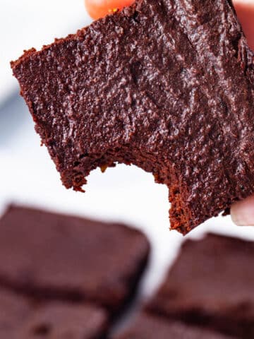 A hand holding a flourless chocolate brownie with a bite taken out of one corner.