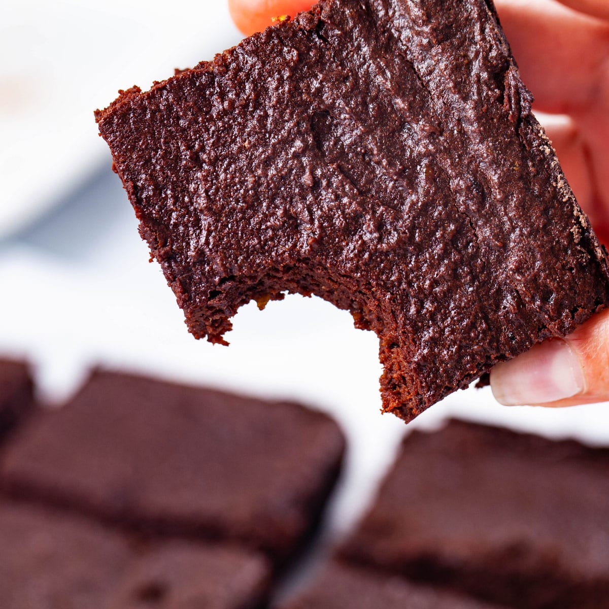A hand holding a flourless chocolate brownie with a bite taken out of one corner.