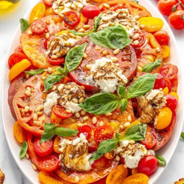 Burrata cheese and tomato salad on a large plate and topped with basil leaves.