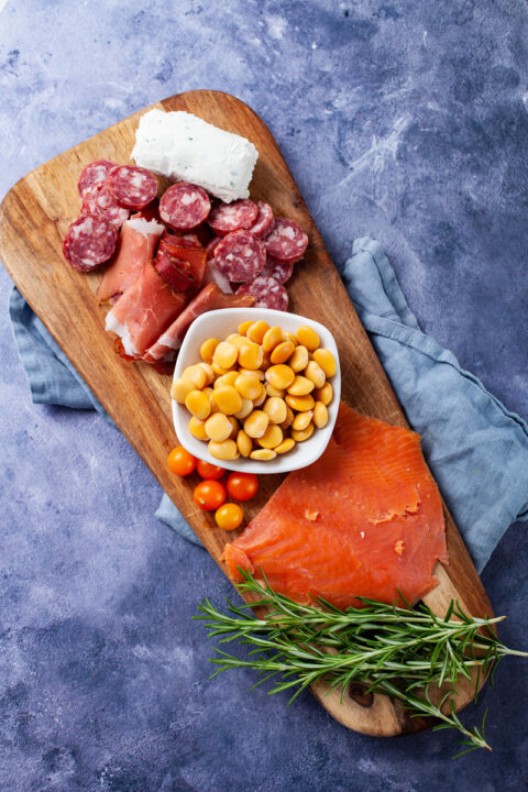 Una exhibición de una tabla de charcutería con carnes, queso, tomates, salmón ahumado y frijoles altramuces.