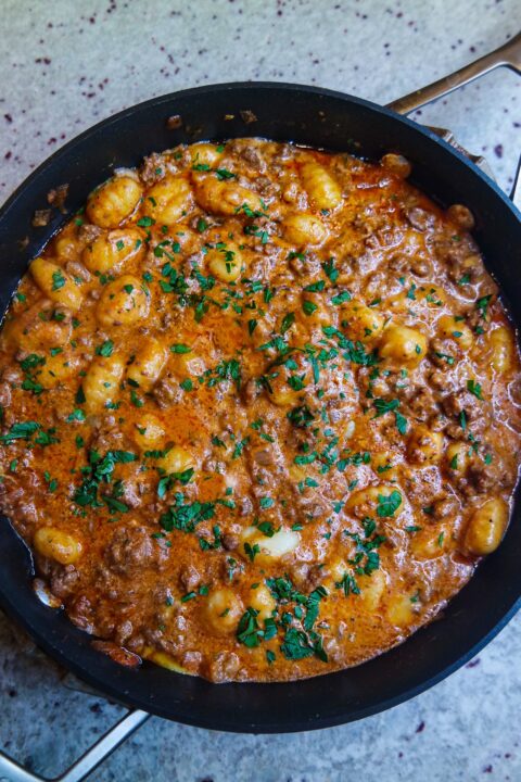 an overhead shot of cheesy bison gnocchi garnished with fresh herbs in a black skillet sitting on a counter top.