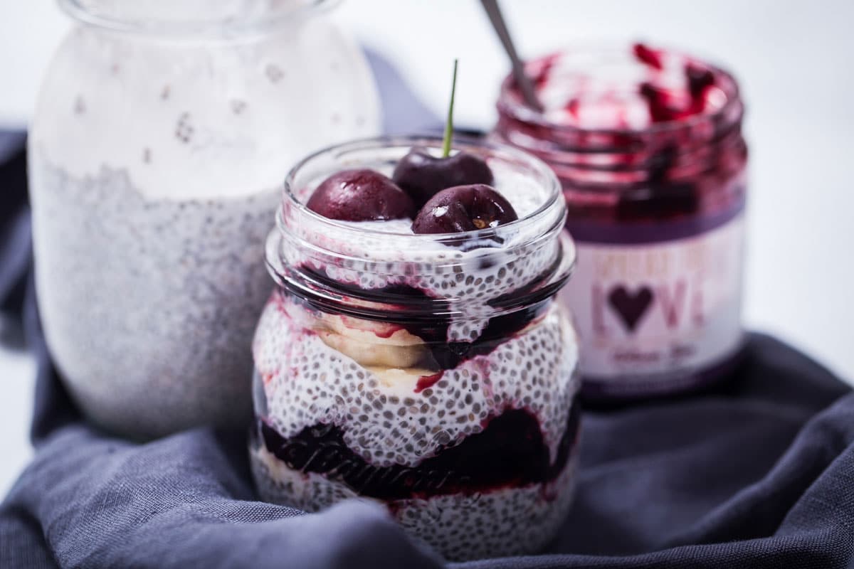Chia seed pudding in a jar layered with berry jam, bananas, and topped with fresh cherries.