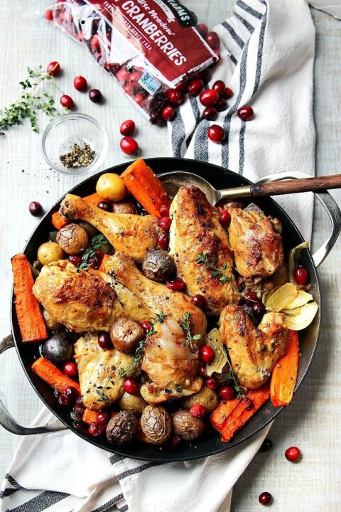 an overhead shot of chicken on a bed of roasted carrots and potatoes with fresh cranberries nestled around.