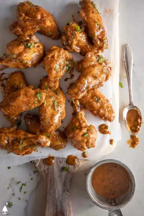an overhead shot of chipotle lime chicken wings on parchment paper on top of a cutting board a bowl and a spoon with dipping sauce on it on the side.
