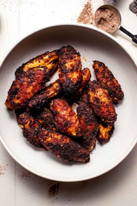 an overhead shot of chicken wings coated in a dry rub on a white dish.