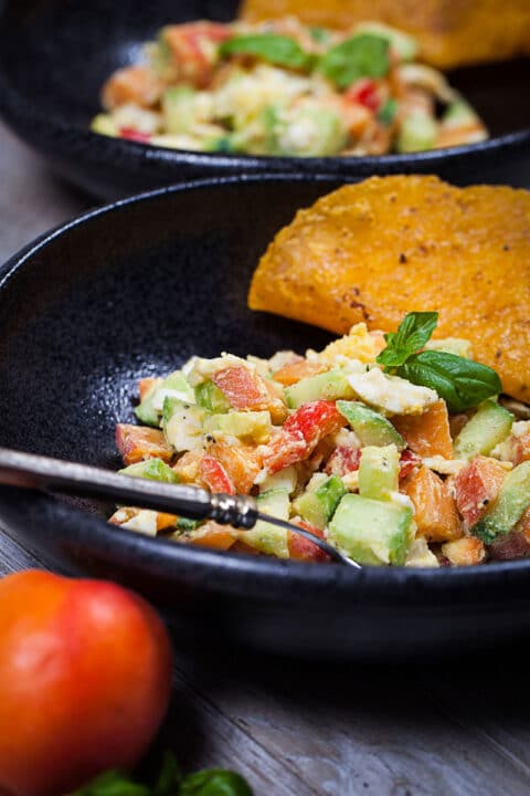 A close up of a bowl filled with a healthy egg salad and apricots with a taco on the side and a fork.