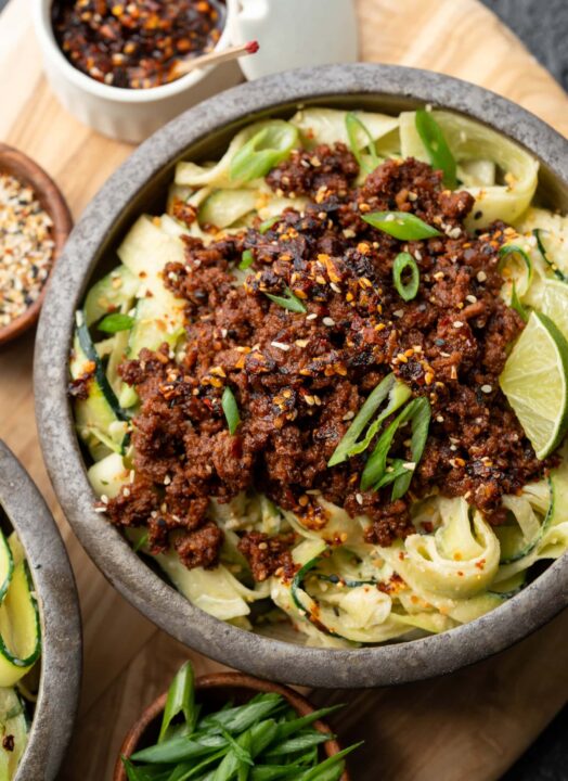 an overhead shot of ground bison on a bed of zucchini noodles with sliced green onions and a wedge of lime as garnish.