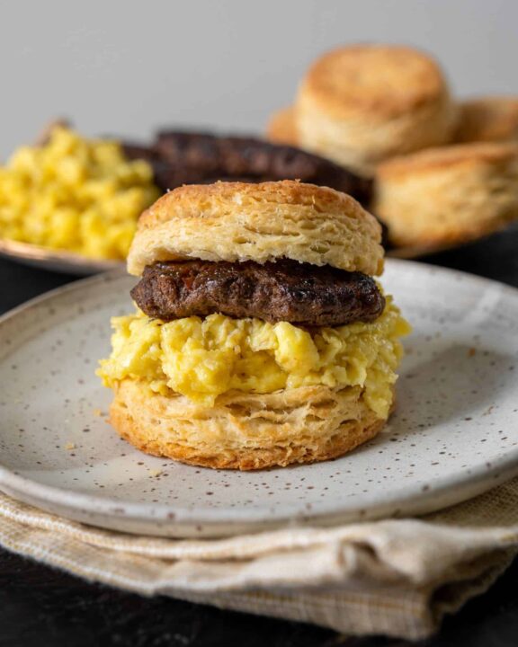 ground bison breakfast sauces and egg on a breakfast biscuit sitting on a speckled white plate.