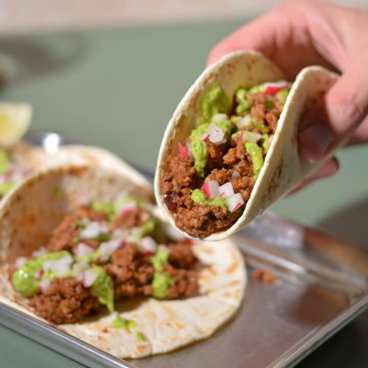 a hand lifting up a ground bison taco garnished with red onions and sauce.