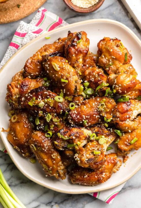 an overhead shot of honey garlic chicken wings on a white plate and the wings are garnished with slices of green onion.