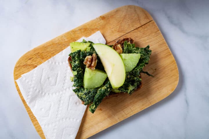 A avocado toast sandwich on a small wooden board.