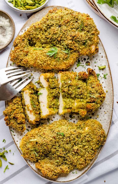 an overhead shot of three pieces of pistachio encrusted chicken on an oval platter.