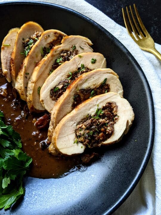 an up close shot of a sliced chicken roulade stuffed with mushrooms and chestnuts on a black plate.
