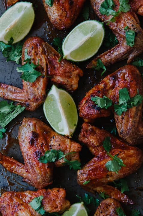 an overhead shot of red curry wings garnished with fresh parsley and beside several lime wedges.