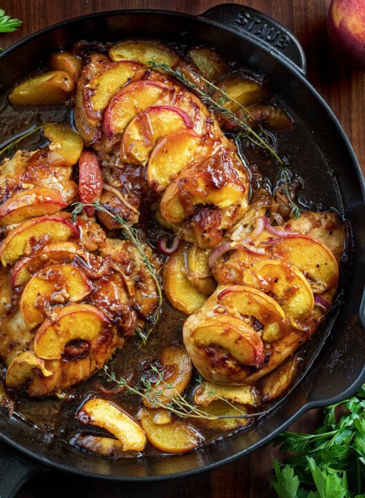 an overhead shot of roasted peach chicken in a cast iron skillet each chicken breast is topped with caramelized slices of peaches.