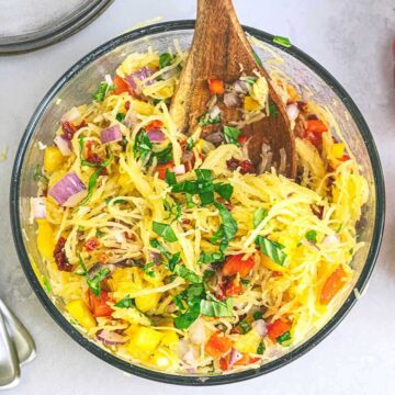 Spaghetti Squash with onions and chopped bell pepper in a large bowl and topped with herbs and a dressing.