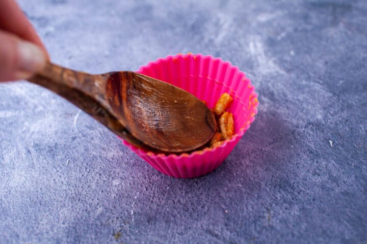 A wooden spoon pressing Kamut cereal in a cupcake holder.