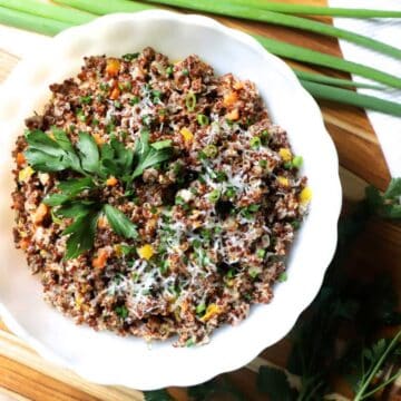 A risotto bowl made from quinoa with a cheesy topping. and filled with finely chopped veggies.