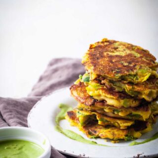 A stack of crispy leek veggie cakes served on a plate with a pesto sauce on the side.